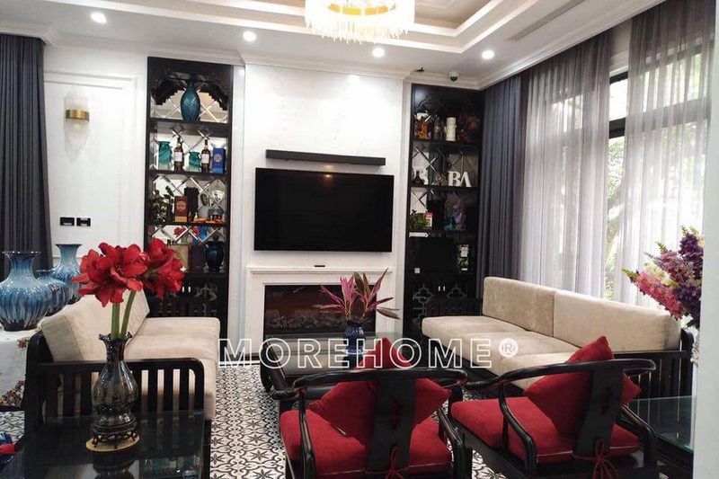 Phòng khách được bố trí nội thất hơi hướng truyền thống với bộ sofa gỗ Việt cao cấp kết hợp với đệm trắng và đệm đỏ tạo nên vẻ đẹp ấm áp cho căn phòng